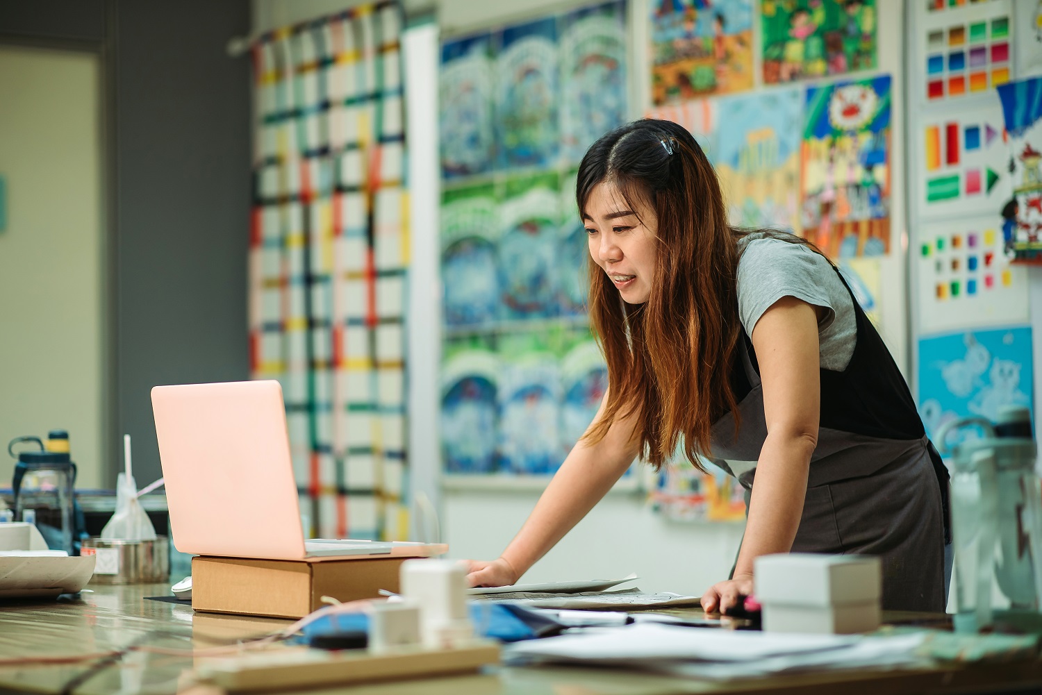 Female art teacher smiling and focusing on her open laptop.