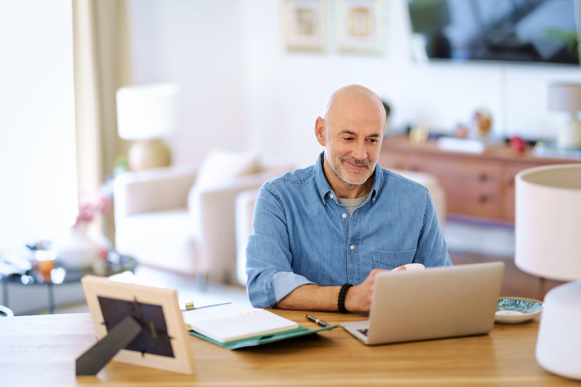 Middle-aged man sitting at a desk smiling at his open laptop.